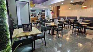 A modern restaurant with a clean, contemporary design, featuring a mix of seating options including tables and booths, and a variety of plants and decorations. - Pazoori Stays at SmartHomes (Nairobi)