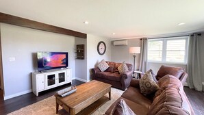 A living room with a television, a brown leather sofa, a wooden coffee table, and a clock on the wall.