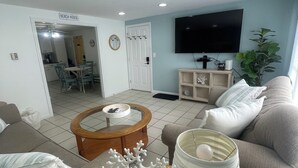 Sala de estar com sofá, mesa de centro, TV e área de jantar com mesa e cadeiras.