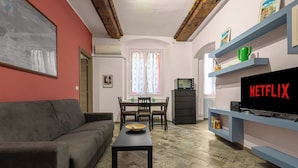 A living room with a sofa, a coffee table, a TV, and a dining area with chairs and a table. - ROSA HOMES - THE GREEN  (Genoa)