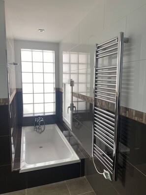 A modern bathroom with a large bathtub, a glass shower enclosure, and a window providing natural light. - VILLA LUCYA (El Campello)