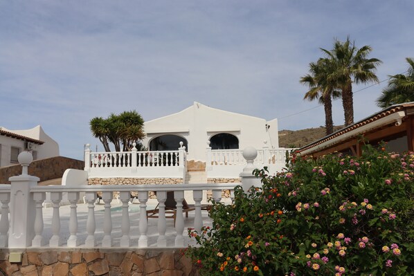 A white building with a balcony, surrounded by stone walls and palm trees. - VILLA LUCYA (El Campello)
