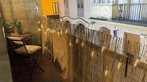 A narrow outdoor corridor with a patterned rug, a chair, a potted plant, and a bamboo fence with hanging lights. - D'Moda lodging. Bright apartment in the center of Ribadeo. (Ribadeo)