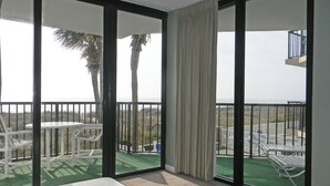 A balcony with a view of the ocean, a white bed, and a table with chairs.