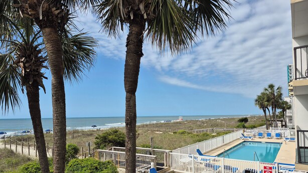 A pool area with blue lounge chairs, a no smoking sign, and a view of the beach and ocean.