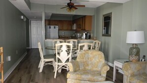 A dining area with a table and chairs, a kitchen in the background, and a ceiling fan.
