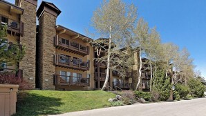 A multi-story hotel with stone and wood exterior, balconies, and a well-maintained lawn. - Beautiful 2 Bedroom + Loft Located in Snowmass (Snowmass Village)