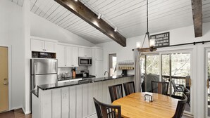 A kitchen with white cabinets, a stainless steel refrigerator, a microwave, and a wooden dining table with chairs. - Beautiful 2 Bedroom + Loft Located in Snowmass (Snowmass Village)