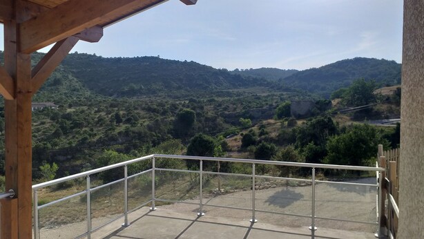 A balcony with a metal railing overlooking a hilly landscape. - We all want to go to the Ardèche! It's great! (Gras)