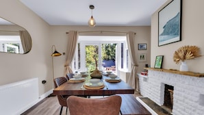 A dining area with a wooden table set for four, a fireplace, and a view of the outdoors. - Oyster Stay House | By My Getaways (Whitstable)