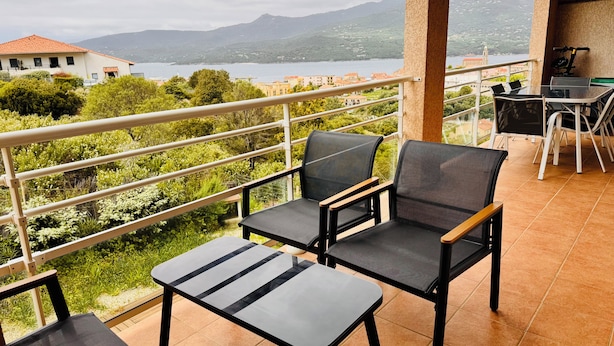 Een balkon met een tafel en twee stoelen, met uitzicht op een prachtig uitzicht van een meer en bergen.