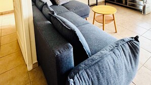 Een moderne woonkamer met een grijze modulaire bank, een klein houten tafeltje, een flatscreen-televisie en kunstwerken aan de muren.