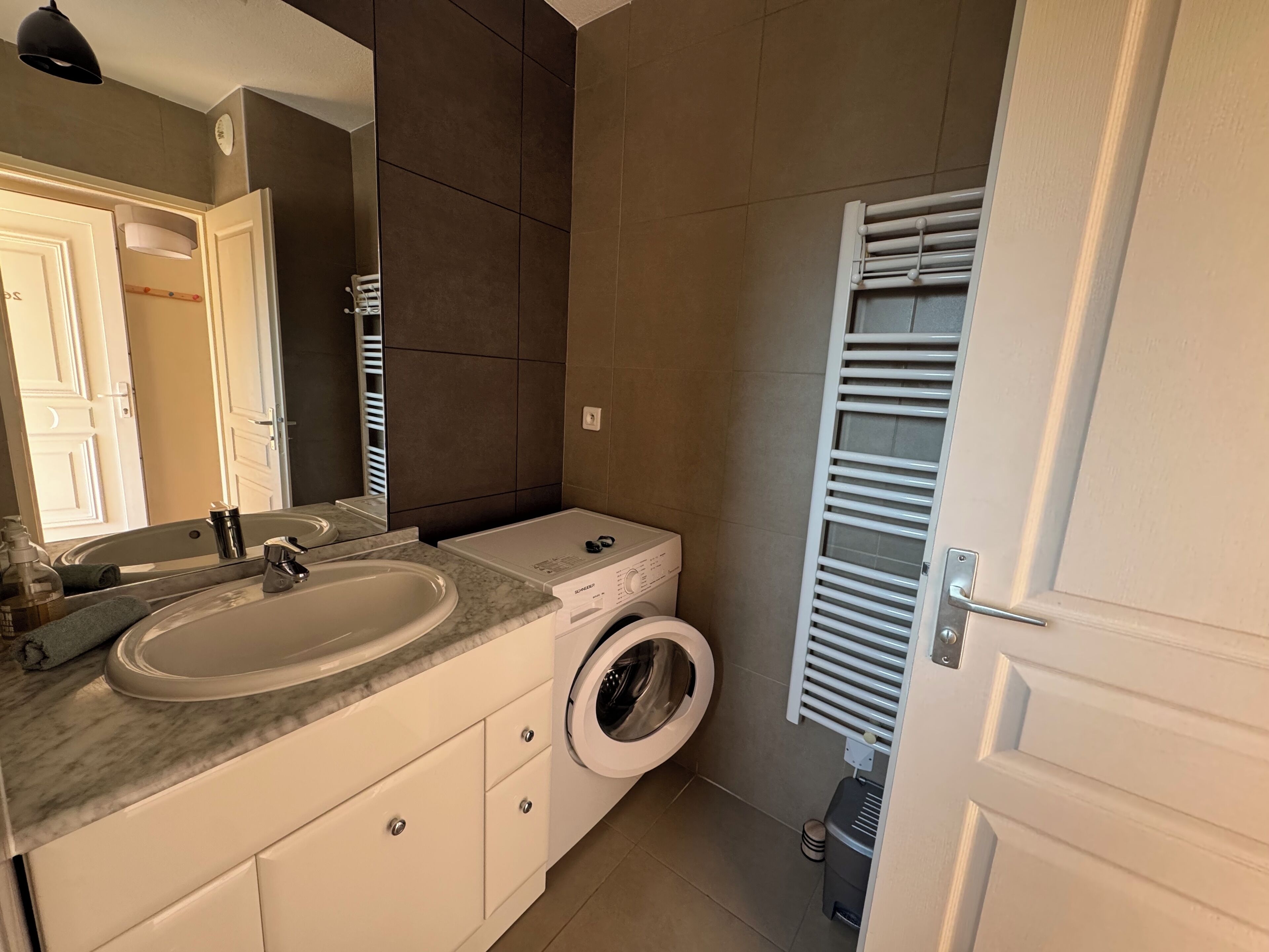 Casa de banho moderna com lavatório, espelho e máquina de lavar roupa embutida.