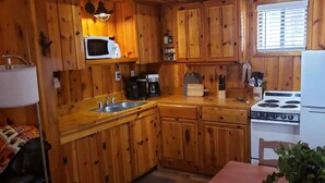 Una cocina compacta con armarios de madera, un microondas, una estufa y un lavamanos.