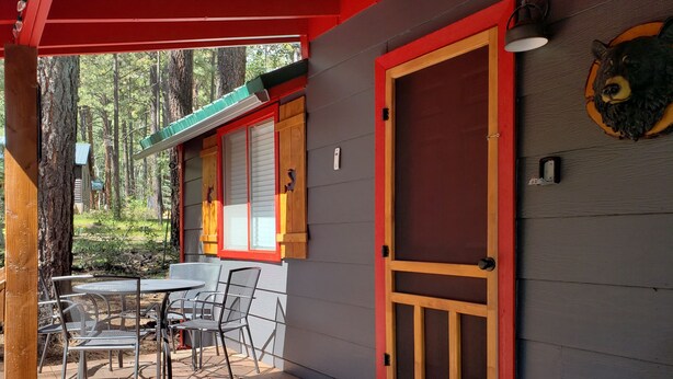 Una terraza de madera con sillas de metal y una mesa, una puerta roja y una decoración de cabeza de oso en la pared.