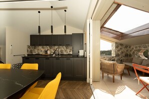 A modern kitchen with dark cabinets, a black countertop, and a dining area with yellow chairs. - Air-conditioned apartment with a terrace in the center of Grimaud, 5 minutes from the ocean. (Grimaud)