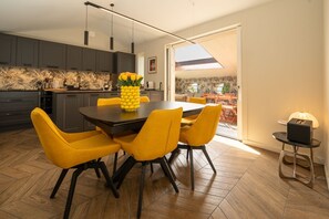 A modern kitchen with dark cabinets, a dining table with yellow chairs, and a view through a glass door to an outdoor area.