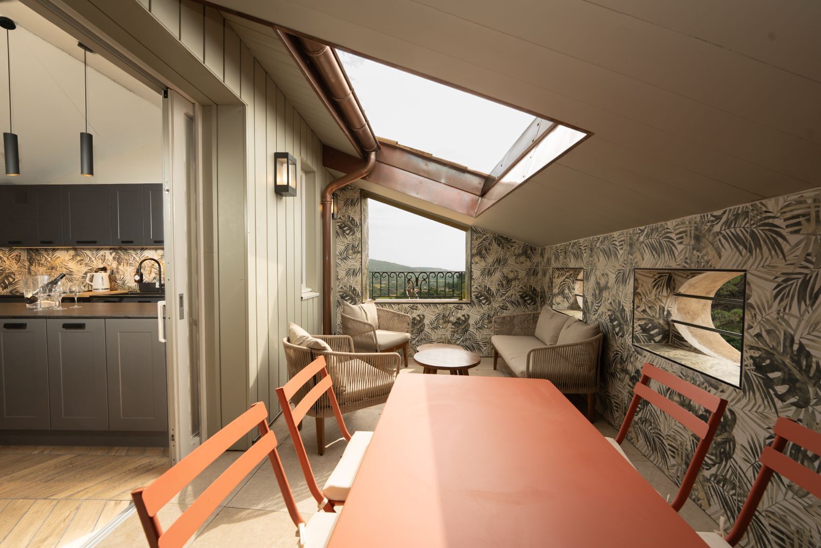 A modern kitchen with a skylight, a dining area with a table and chairs, and a living space with a sofa and a view of the outdoors.