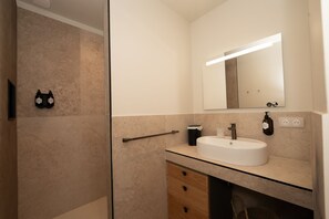 A bathroom with a glass shower enclosure, a white sink, a mirror, and a towel rack.
