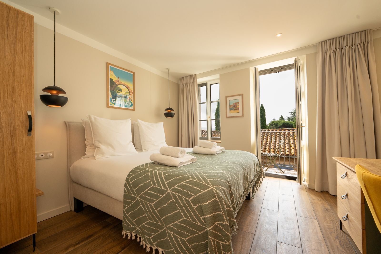 Habitación de hotel con cama, escritorio, balcón con barandilla y un cuadro en la pared.