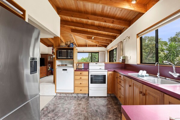Una cocina moderna con un refrigerador de acero inoxidable, electrodomésticos blancos, armarios de madera y un ventanal con vistas a zonas verdes.