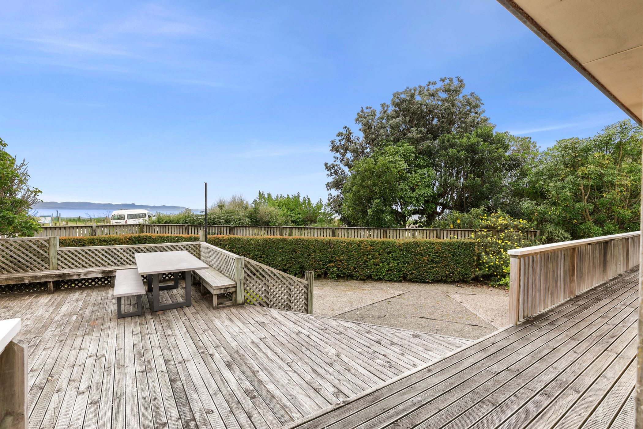 A wooden deck with a table and benches, surrounded by a wooden fence and greenery.