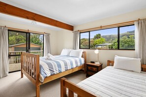 A bedroom with two beds, a nightstand, and a window with a view of greenery and hills.