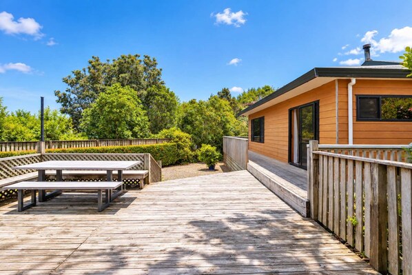 A wooden deck with picnic tables, a small building with a sloped roof, and a wooden fence.