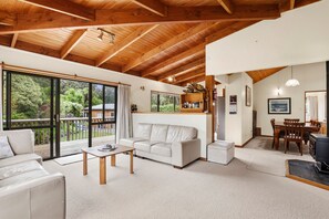 A spacious living area with a wooden ceiling, a white sofa, a coffee table, and a dining table with chairs.