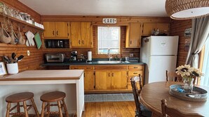 Una cucina con mobili in legno, un lavello, un fornello e un frigorifero. Ci sono due sgabelli di legno e un tavolo con un vaso di fiori.