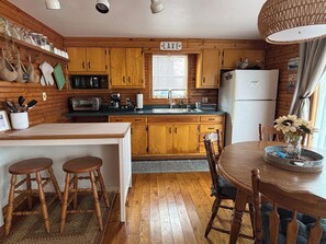 A kitchen with wooden cabinets, a sink, a stove, and a refrigerator. There are two wooden stools and a table with a vase of flowers.