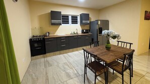 A modern kitchen with dark cabinets, a built-in oven, and a refrigerator. There is a dining table with chairs and a vase of flowers. - ZEMMA Apartments Unit 2 (Willemstad)