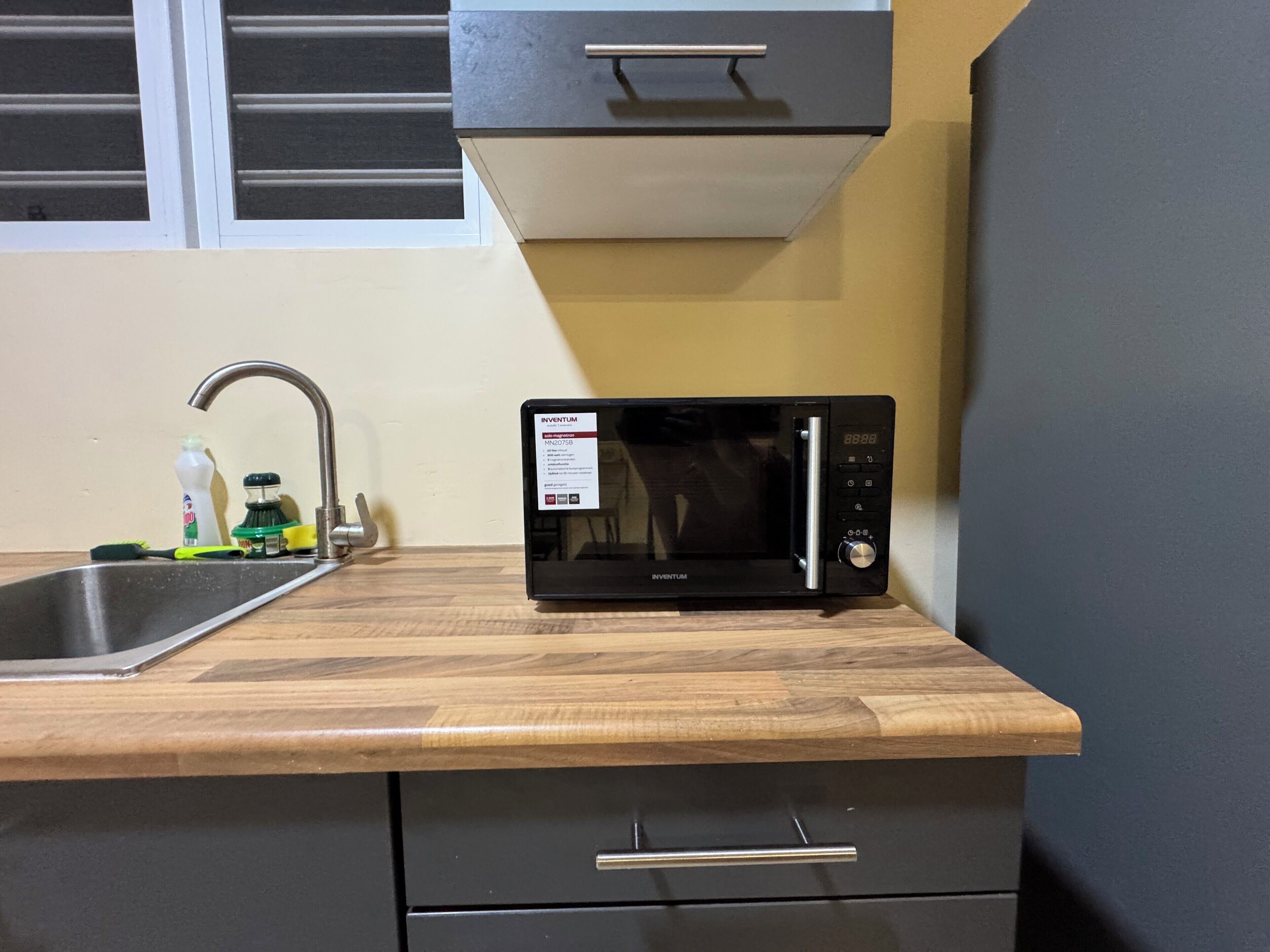A kitchen with a black microwave on a wooden countertop, a stainless steel sink, and a window above the sink.