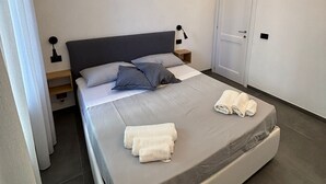 A modern bedroom with a large bed, a bedside table, a lamp, and a door.