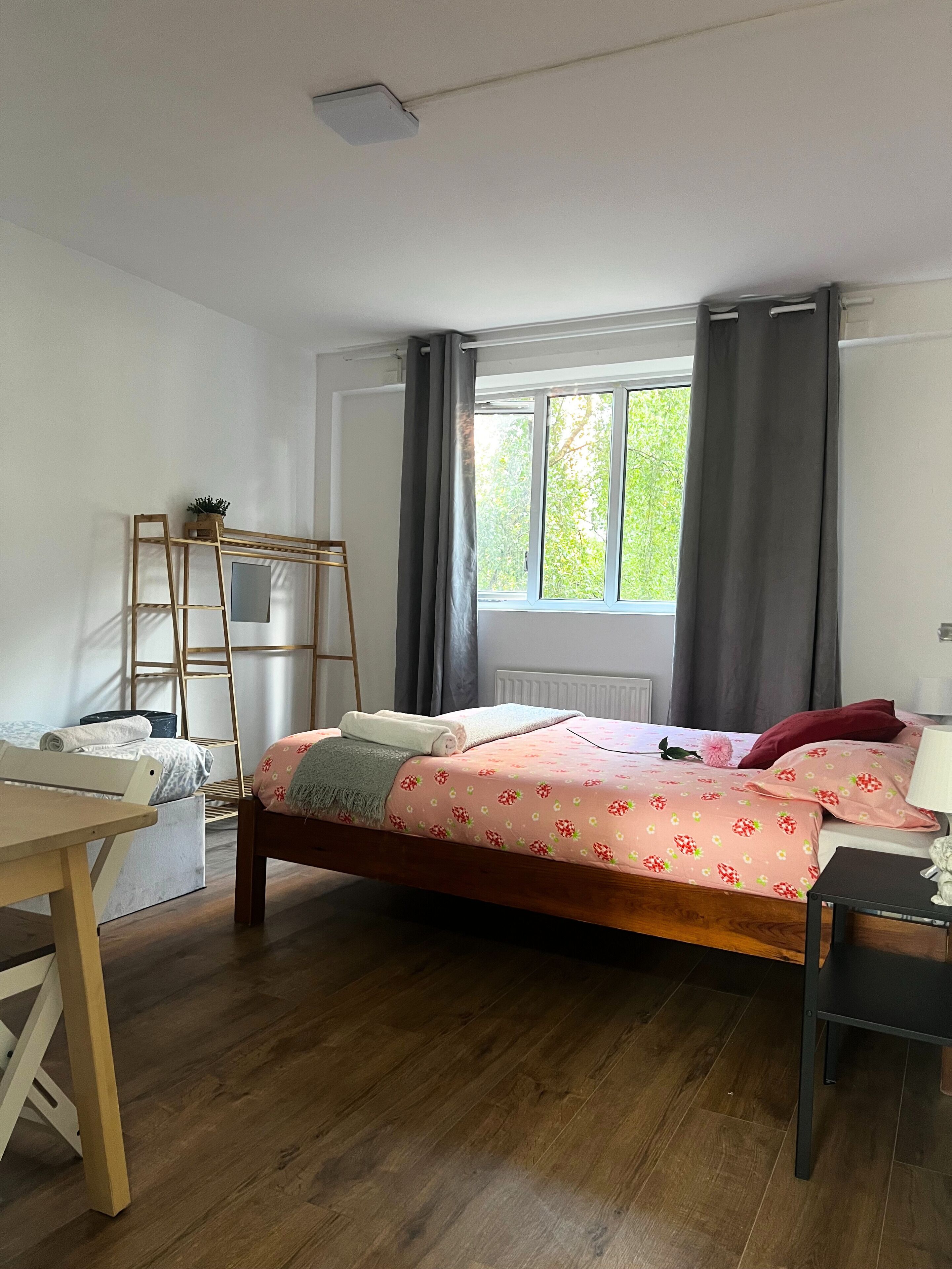 A bedroom with a wooden bed, a desk, a ladder, and a window with curtains.