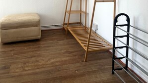 Una habitación de esquina con un estante de madera escalonado, un pequeño reposapiés beige y un perchero metálico en la pared.