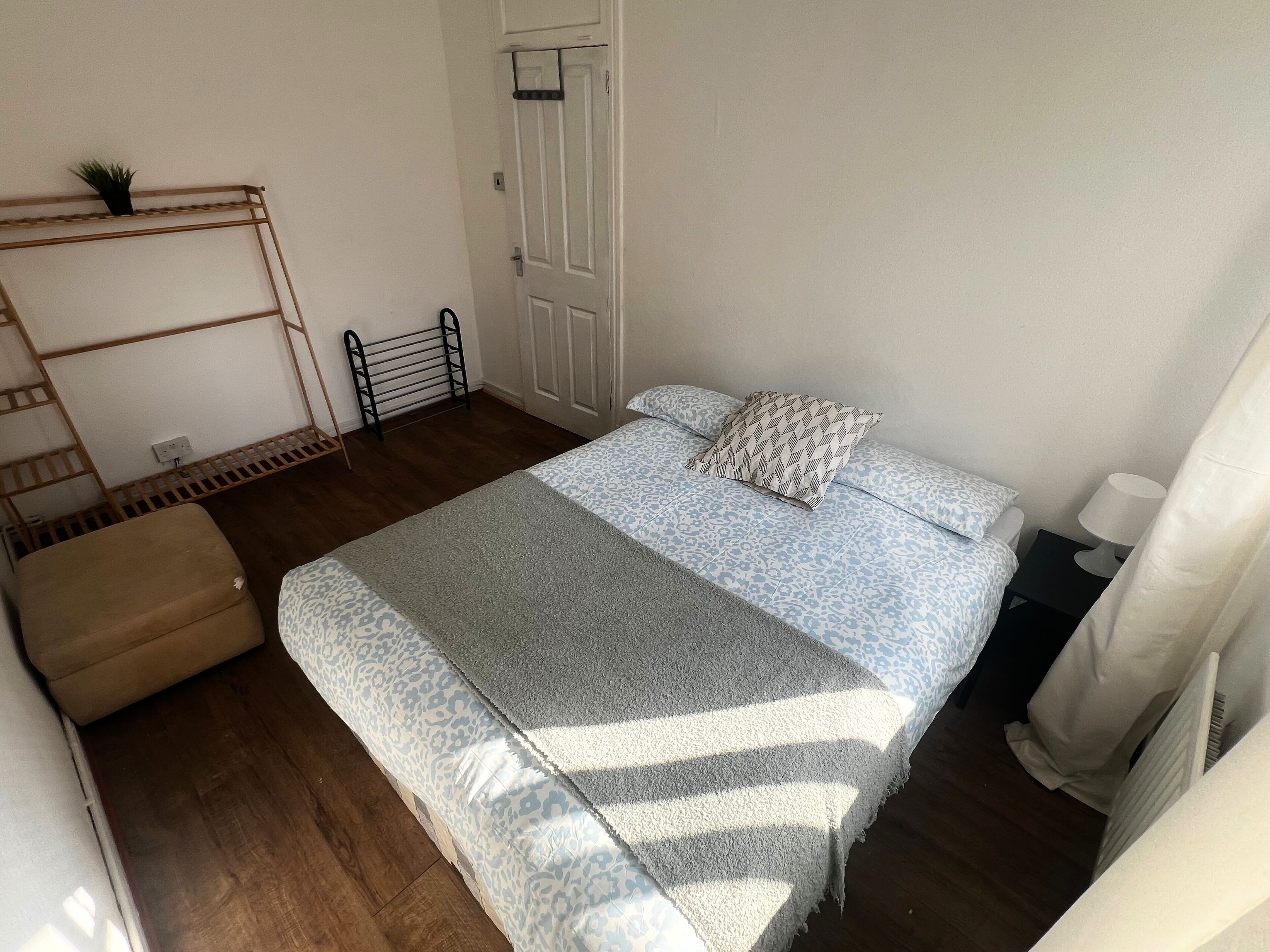 Quarto com uma cama, uma pequena mesa de cabeceira, um radiador, uma escada de madeira e uma porta.