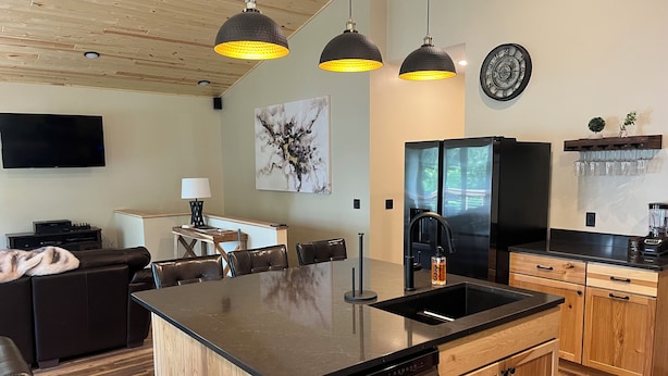 Una cocina moderna con una isla central, electrodomésticos negros, armarios de madera e iluminación colgante.