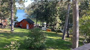 Una cabaña con un muelle, rodeada de árboles y un área cubierta de césped.