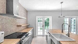Een moderne keuken met een inbouwoven, een RVS kookplaat, een dubbele spoelbak en een houten aanrechtblad.
