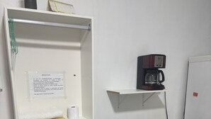 Een compacte kamer met een bureau, twee stoelen, een koffiezetapparaat en een kleine potplant.