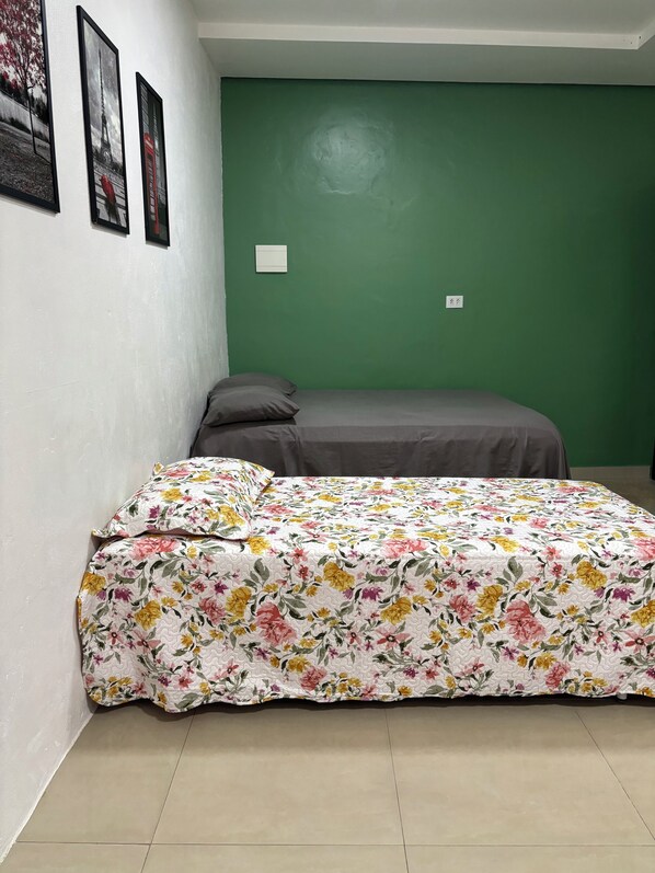 A bedroom with a green wall, a bed with a floral bedspread, and three framed pictures on the wall.
