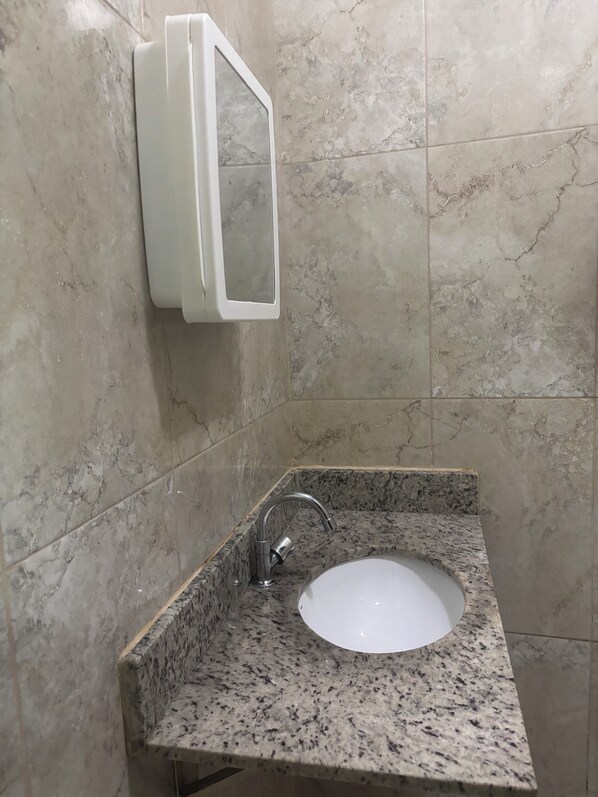 A bathroom with a granite countertop sink, a white medicine cabinet, and a marble-tiled wall.