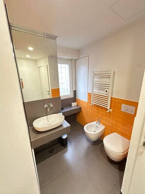 Une salle de bain moderne avec un grand miroir, un lavabo, un bidet et des toilettes.