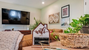 Ett vardagsrum med en platt-TV, en soffa, ett soffbord med en dekorativ detalj och en skylt med texten ”wifi”.
