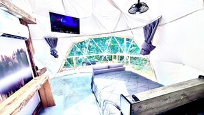 Ein Zelt mit einem Bett, einem Fernseher und Blick auf Bäume.