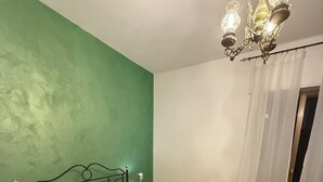 A room with a bed, green walls, a chandelier, and a wooden floor.