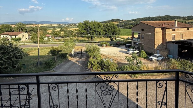 A balcony with a wrought iron railing overlooking a rural landscape with houses, a road, and fields.