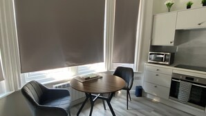 Cocina moderna con microondas, horno y armarios. Hay una mesa de comedor con sillas y una ventana con persianas.