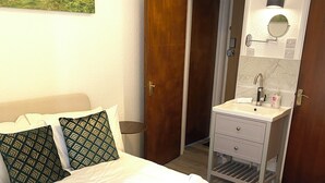 Habitación de hotel con cama, baño con lavamanos y espejo, y una puerta que da a otra habitación.
